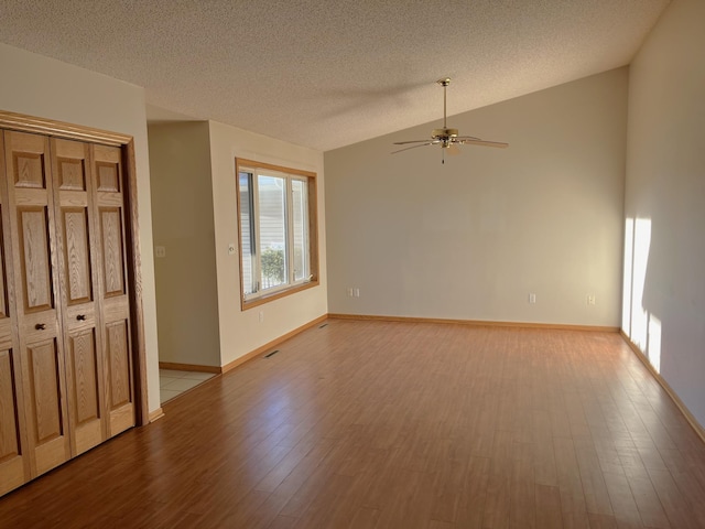 unfurnished room featuring ceiling fan, lofted ceiling, a textured ceiling, and light hardwood / wood-style flooring