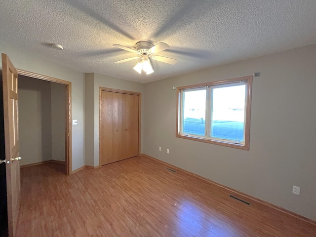 unfurnished bedroom with ceiling fan, a closet, a textured ceiling, and light wood-type flooring