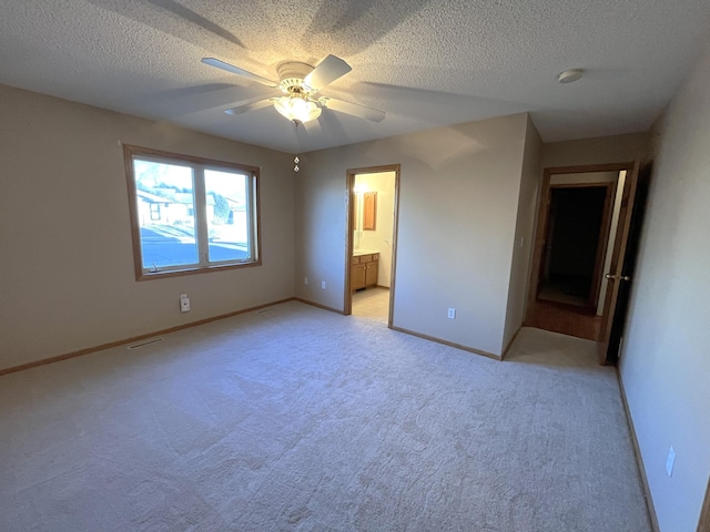 unfurnished bedroom with a textured ceiling, light colored carpet, ensuite bath, and ceiling fan