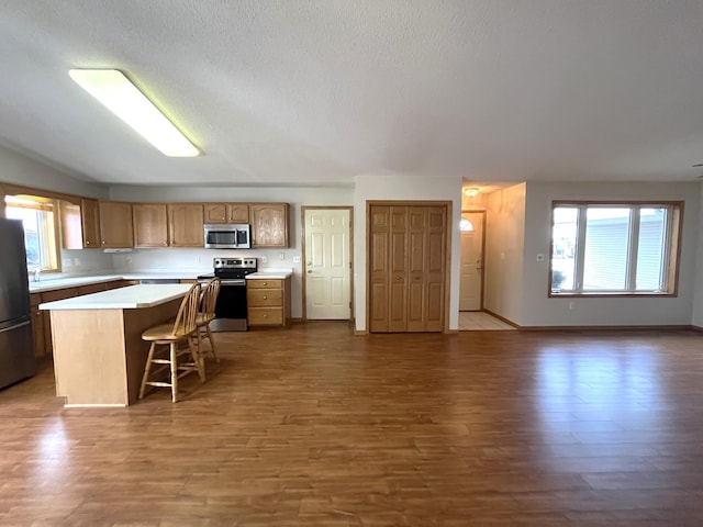 kitchen featuring a kitchen bar, appliances with stainless steel finishes, a textured ceiling, hardwood / wood-style floors, and a center island