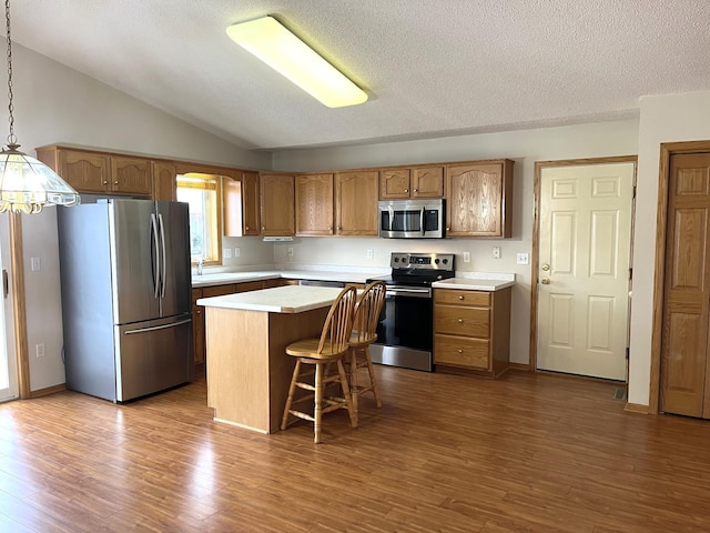 kitchen with lofted ceiling, appliances with stainless steel finishes, decorative light fixtures, a kitchen island, and a breakfast bar area