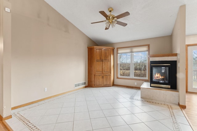 unfurnished living room with a tiled fireplace, ceiling fan, light tile patterned floors, and vaulted ceiling