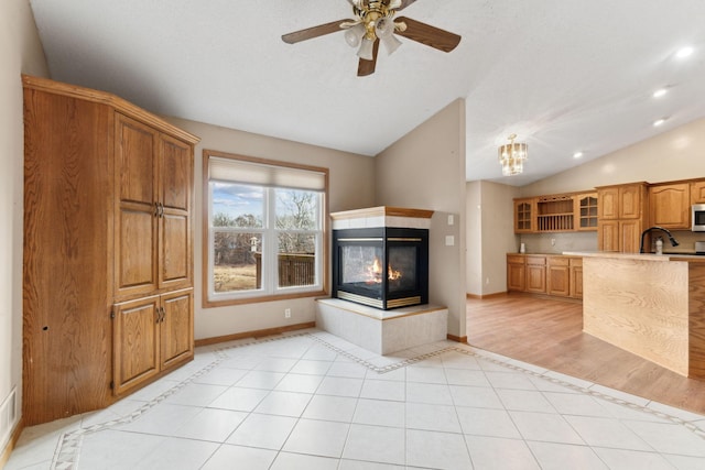 kitchen with vaulted ceiling, ceiling fan, sink, light tile patterned floors, and a fireplace