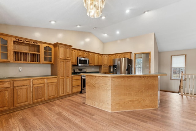 kitchen featuring light wood-type flooring, stainless steel appliances, high vaulted ceiling, a chandelier, and an island with sink