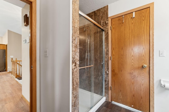 bathroom with hardwood / wood-style flooring, a shower with shower door, and a textured ceiling