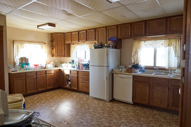 kitchen with brown cabinetry, plenty of natural light, white appliances, and a sink