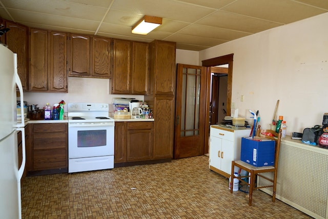 kitchen featuring brown cabinetry, white appliances, light countertops, and a drop ceiling