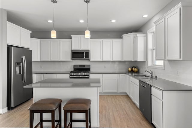 kitchen with a center island, decorative light fixtures, white cabinetry, stainless steel appliances, and sink