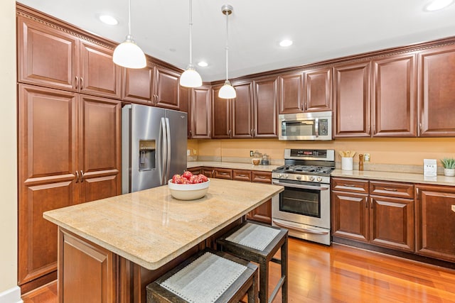 kitchen featuring a center island, stainless steel appliances, pendant lighting, light hardwood / wood-style floors, and a breakfast bar