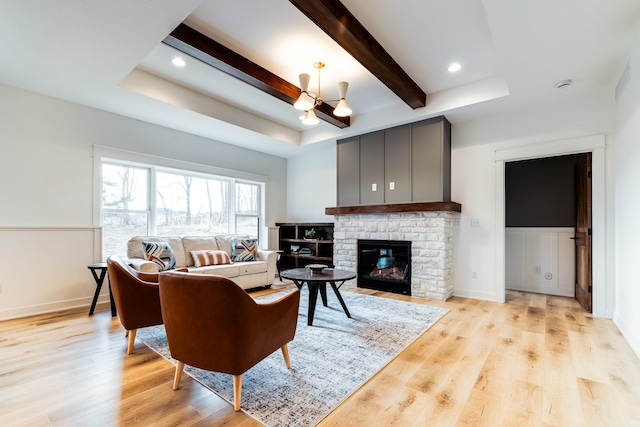 living room with a raised ceiling, a fireplace, a notable chandelier, and light hardwood / wood-style floors