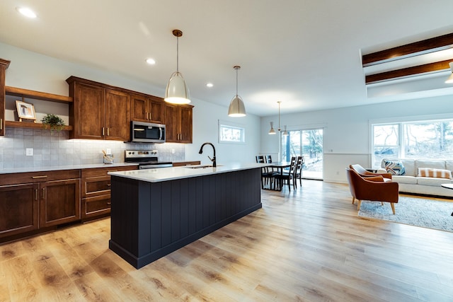 kitchen featuring decorative light fixtures, sink, light hardwood / wood-style flooring, an island with sink, and stainless steel appliances