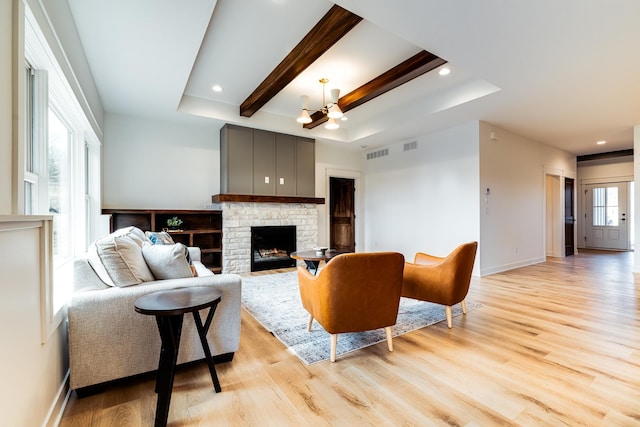 living area featuring light wood-style flooring, a chandelier, a fireplace, baseboards, and beamed ceiling