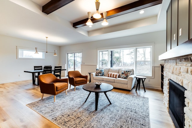 living room featuring beamed ceiling, light wood-style flooring, a stone fireplace, and baseboards