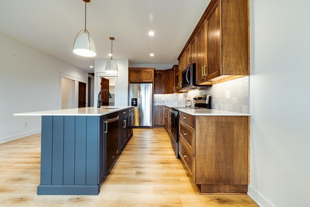 kitchen with appliances with stainless steel finishes, a sink, a center island with sink, light countertops, and recessed lighting