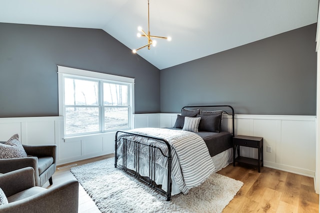 bedroom with a chandelier, a decorative wall, a wainscoted wall, light wood-type flooring, and vaulted ceiling