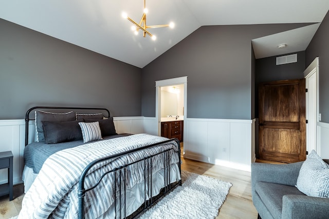 bedroom with a wainscoted wall, light wood-style floors, a chandelier, high vaulted ceiling, and connected bathroom