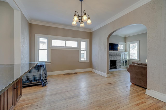 foyer entrance featuring a brick fireplace, light hardwood / wood-style flooring, ornamental molding, and a chandelier