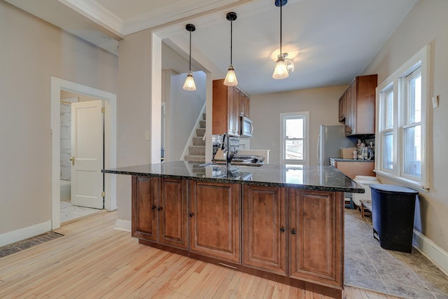 kitchen with decorative light fixtures, sink, light wood-type flooring, stainless steel appliances, and dark stone counters