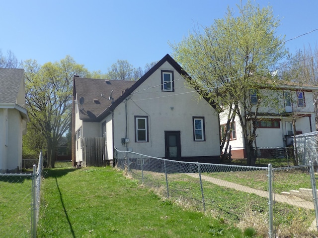 back of house with a lawn, fence private yard, roof with shingles, and stucco siding
