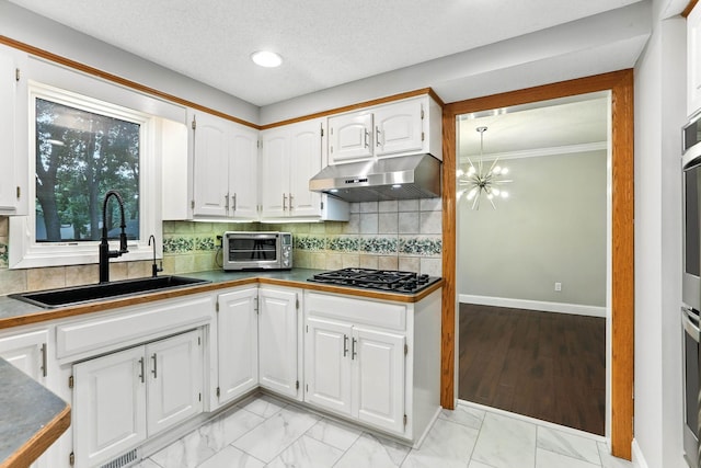 8385 Pleasant View Dr, Mounds View, MN 55112 - kitchen featuring under cabinet range hood, stainless steel gas cooktop, white cabinets, decorative backsplash, and crown molding