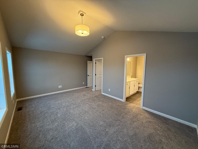 unfurnished bedroom featuring dark carpet, connected bathroom, and lofted ceiling