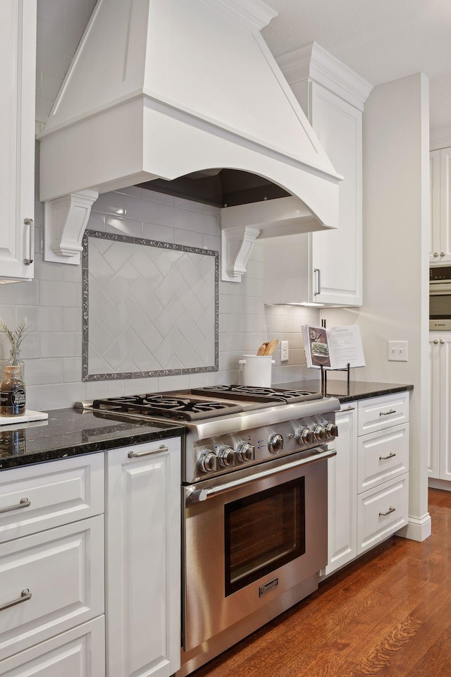 kitchen featuring premium range hood, backsplash, white cabinetry, and high end range