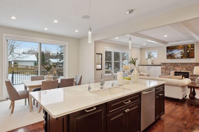 kitchen with sink, hanging light fixtures, dark wood-type flooring, a stone fireplace, and an island with sink