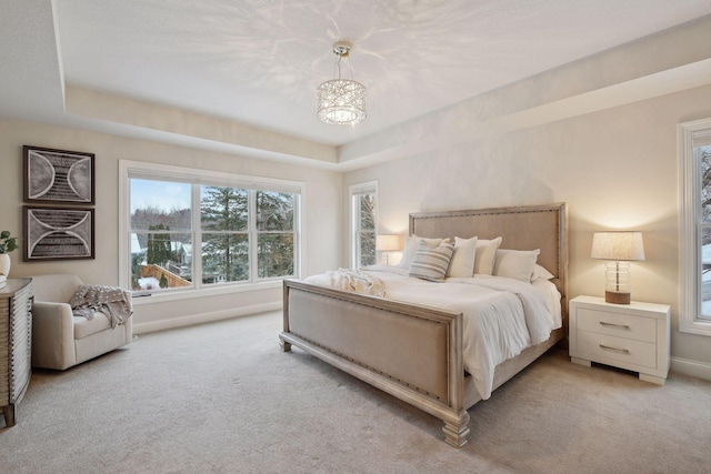 bedroom featuring an inviting chandelier, light colored carpet, and a tray ceiling