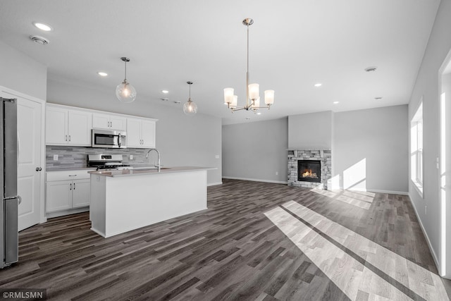 kitchen featuring a fireplace, white cabinets, appliances with stainless steel finishes, and an island with sink