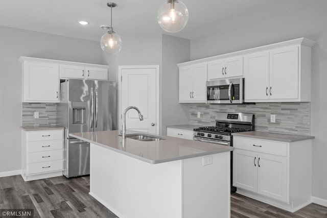 kitchen with pendant lighting, appliances with stainless steel finishes, white cabinetry, an island with sink, and sink