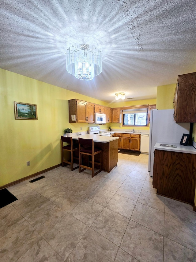 kitchen featuring white appliances, a kitchen breakfast bar, sink, light tile patterned floors, and kitchen peninsula