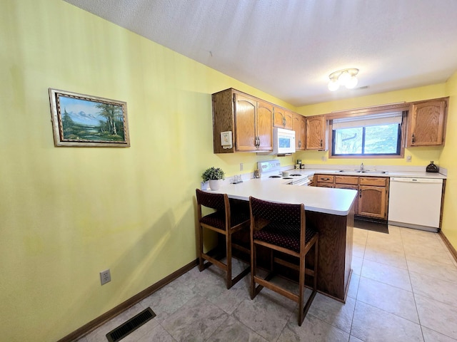 kitchen featuring a breakfast bar, white appliances, sink, light tile patterned floors, and kitchen peninsula