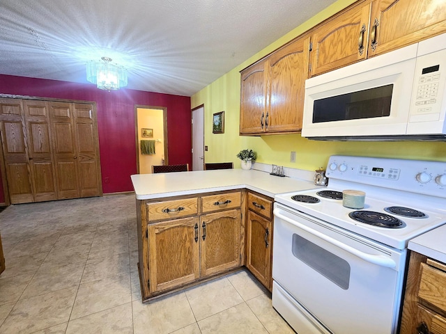 kitchen featuring kitchen peninsula, white appliances, a chandelier, and light tile patterned flooring