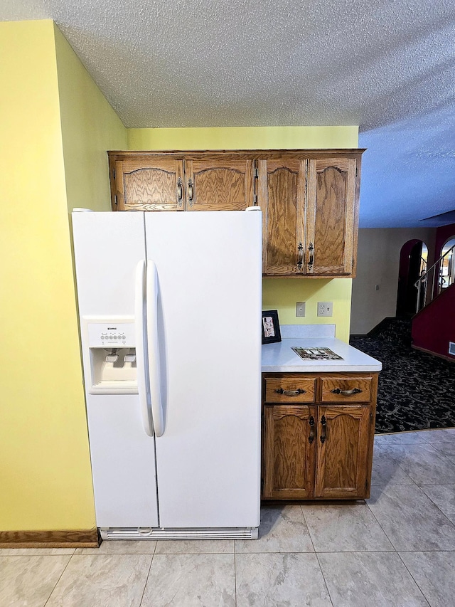 kitchen featuring white fridge with ice dispenser, light tile patterned floors, and a textured ceiling