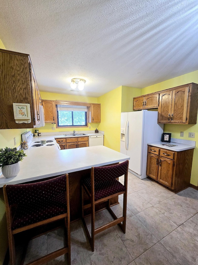 kitchen featuring white appliances, sink, light tile patterned floors, a textured ceiling, and kitchen peninsula