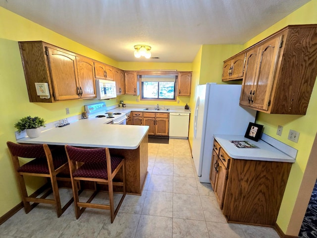 kitchen featuring light tile patterned flooring, a breakfast bar, sink, kitchen peninsula, and white appliances