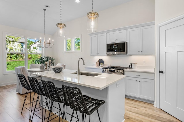 kitchen featuring white cabinets, appliances with stainless steel finishes, sink, hanging light fixtures, and a center island with sink