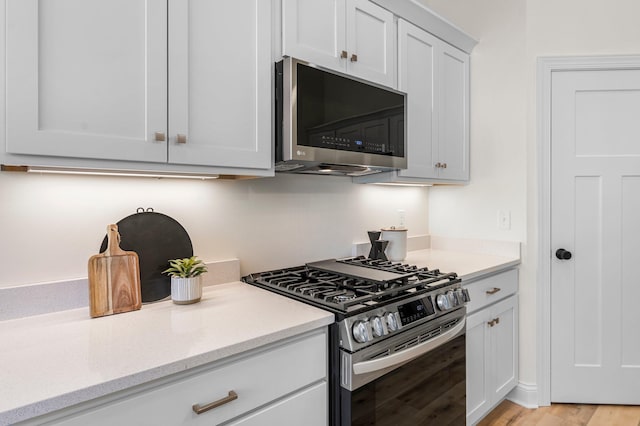 kitchen with white cabinets, light stone countertops, stainless steel appliances, and light hardwood / wood-style flooring