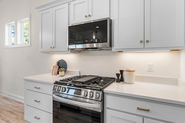 kitchen with light wood-type flooring, appliances with stainless steel finishes, and white cabinets