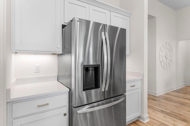 kitchen with stainless steel refrigerator with ice dispenser, white cabinetry, light hardwood / wood-style floors, and light stone counters