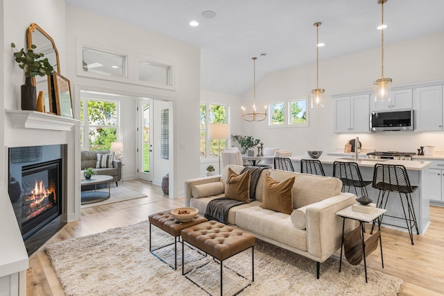 living room featuring light wood-type flooring, a chandelier, vaulted ceiling, and sink