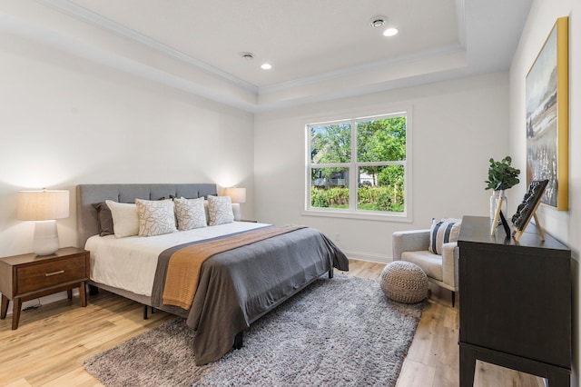 bedroom with ornamental molding, light hardwood / wood-style floors, and a tray ceiling