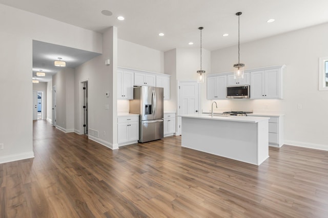 kitchen with appliances with stainless steel finishes, pendant lighting, white cabinets, and an island with sink