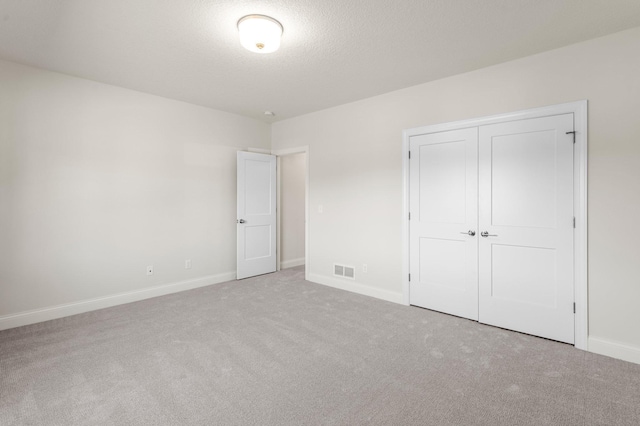 unfurnished bedroom with a textured ceiling, a closet, and light carpet