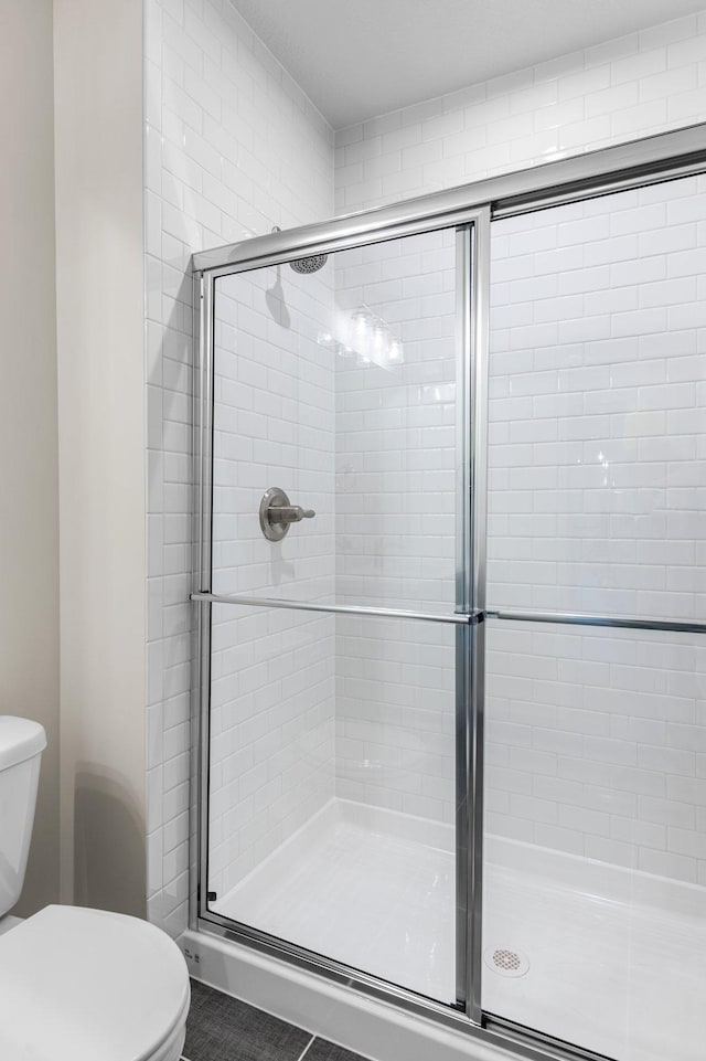 bathroom featuring an enclosed shower, tile patterned floors, and toilet