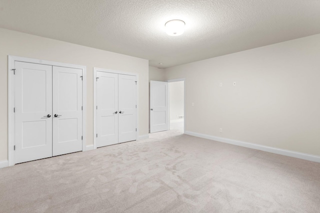 unfurnished bedroom featuring light carpet, multiple closets, and a textured ceiling