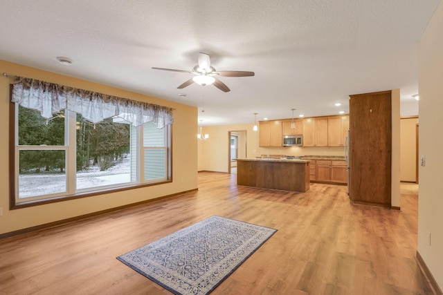 kitchen with ceiling fan with notable chandelier, a kitchen island, light hardwood / wood-style floors, and decorative light fixtures