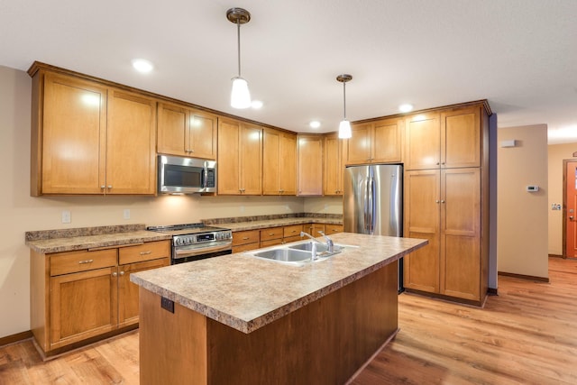 kitchen featuring appliances with stainless steel finishes, light wood-type flooring, sink, a center island with sink, and hanging light fixtures