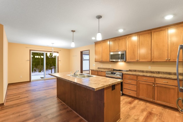 kitchen featuring stainless steel appliances, sink, decorative light fixtures, a center island with sink, and light hardwood / wood-style floors