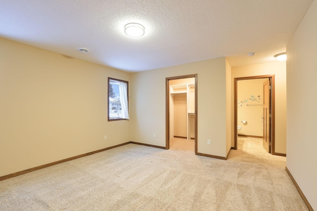 unfurnished bedroom featuring a textured ceiling, a walk in closet, light colored carpet, and a closet